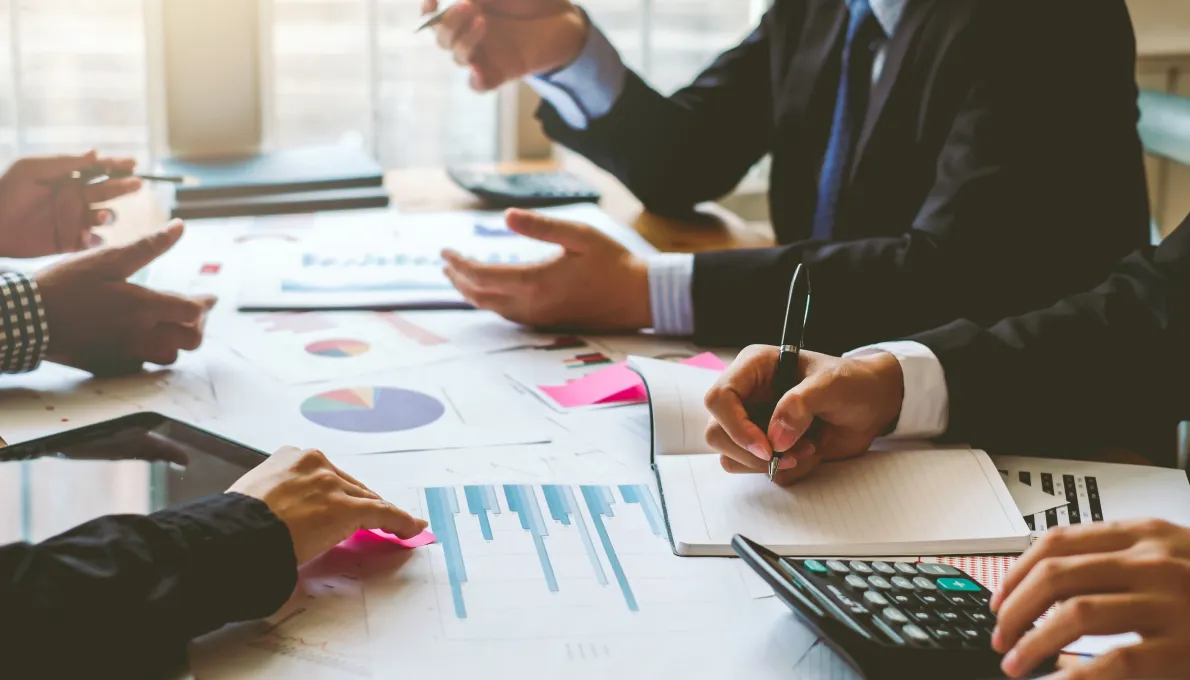 analisis-financiero-equipo Manos de ejecutivos colaboran en una reunión de negocios analizando gráficos de datos, tomando notas y usando una calculadora para la planificación financiera.