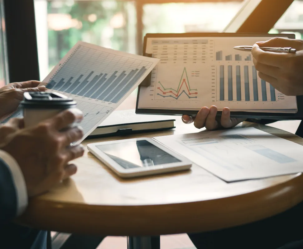 analisis-negocio-graficos Manos de ejecutivos colaboran en una reunión de negocios analizando gráficos de datos, tomando notas y usando una calculadora para la planificación financiera.